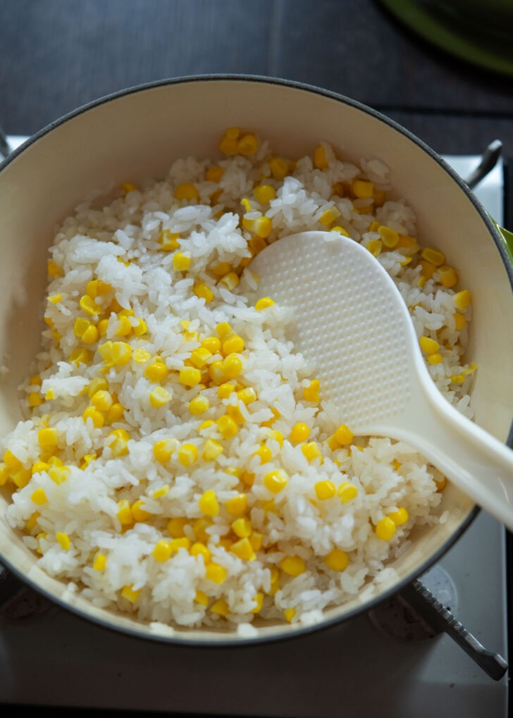 A rice paddle mixing up corn rice in a pot