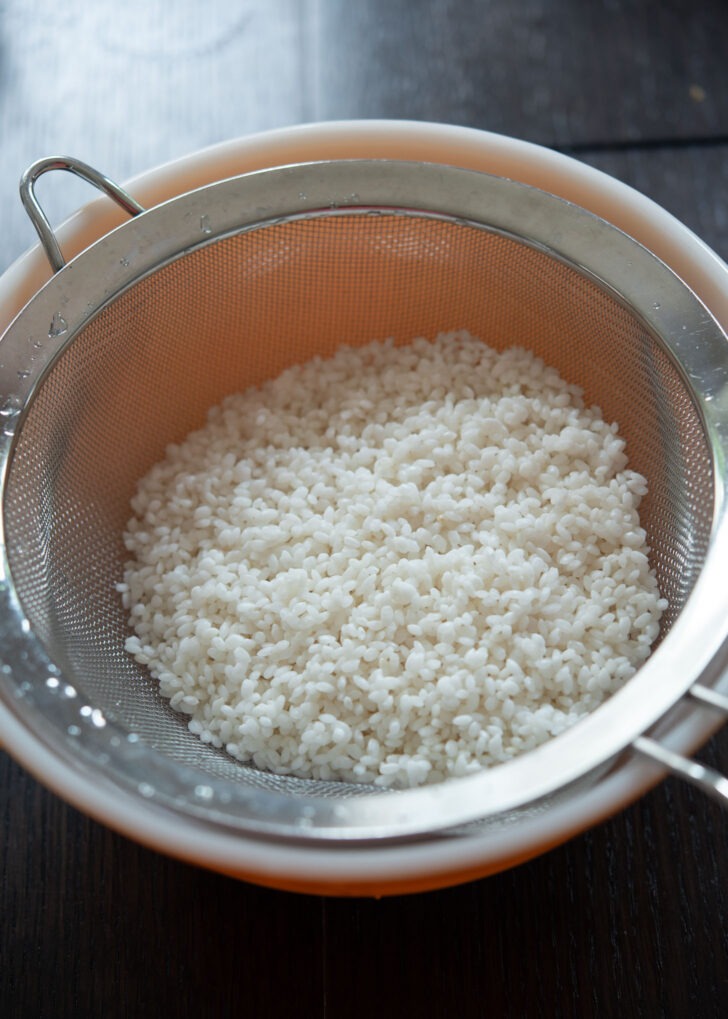 Soaked rice being drained in a colander.
