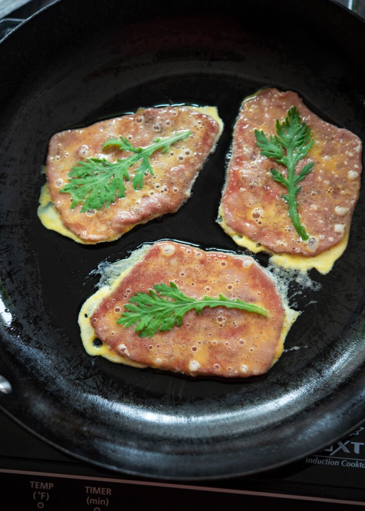 Egg battered beef pancake garnished with crown daisy in a killet