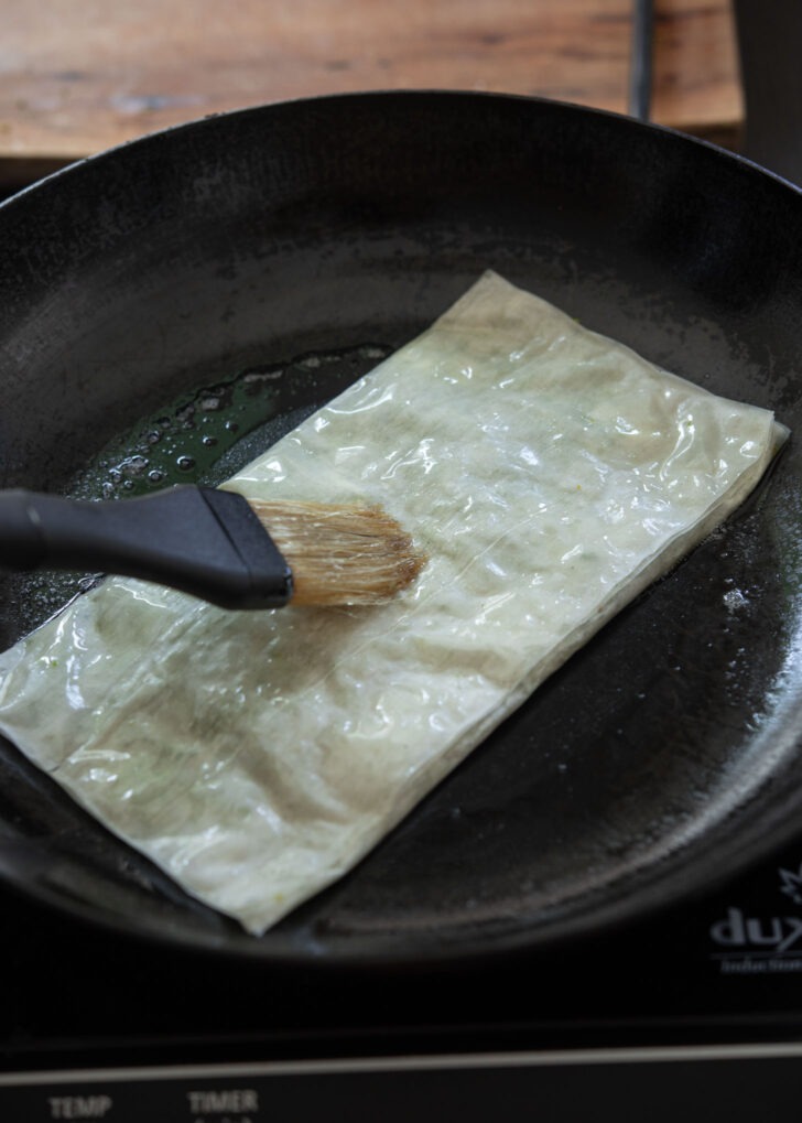 Brushing with melted butter on the top side of Katmer pastry in a skillet.
