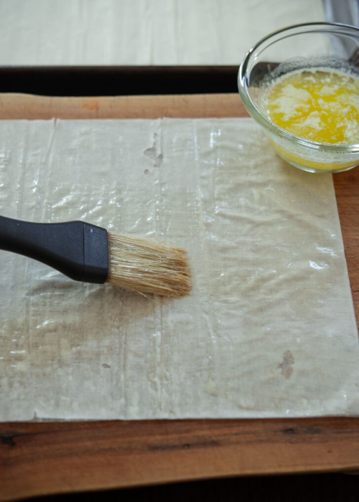 A pastry brush applying melted butter on filo pastry sheet.