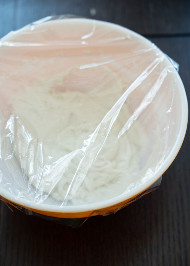 A plastic wrap covers the sweet rice cake dough in a bowl.