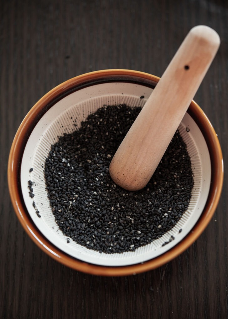 Black sesame seeds grinding in a small suribachi mortar with pestle.