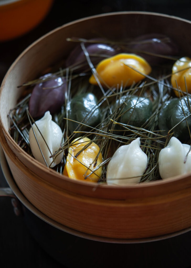 Various colored songpyeon steamed in a bamboo basket.