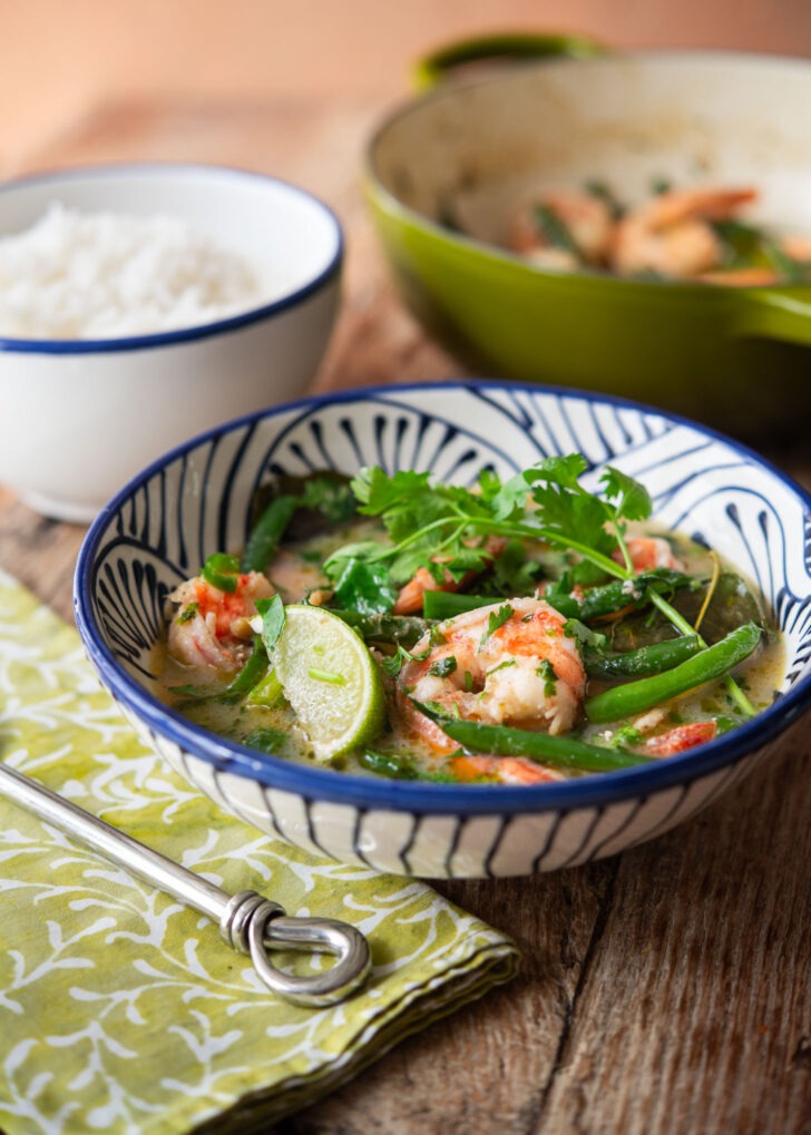 A bowl of green curry shrimp with green beans served with rice.