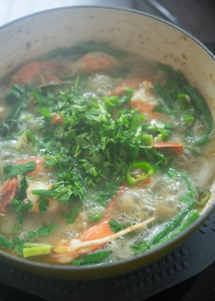 Fresh green chili and cilantro added to simmering green curry shrimp in a pot.