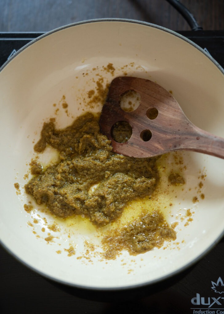Green curry paste is frying in oil in a pan.