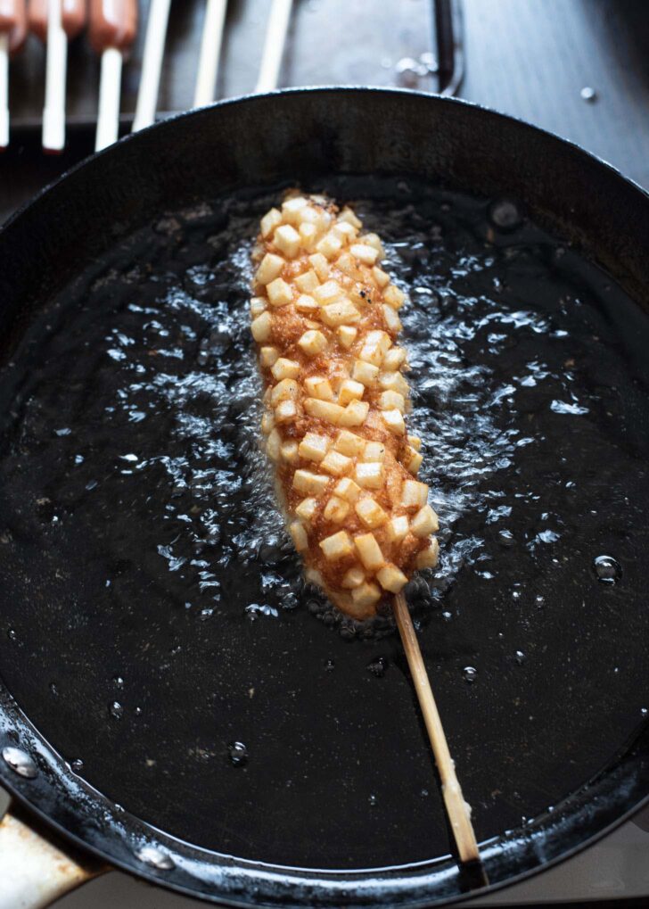 Potato corn dog deep frying in hot oil.