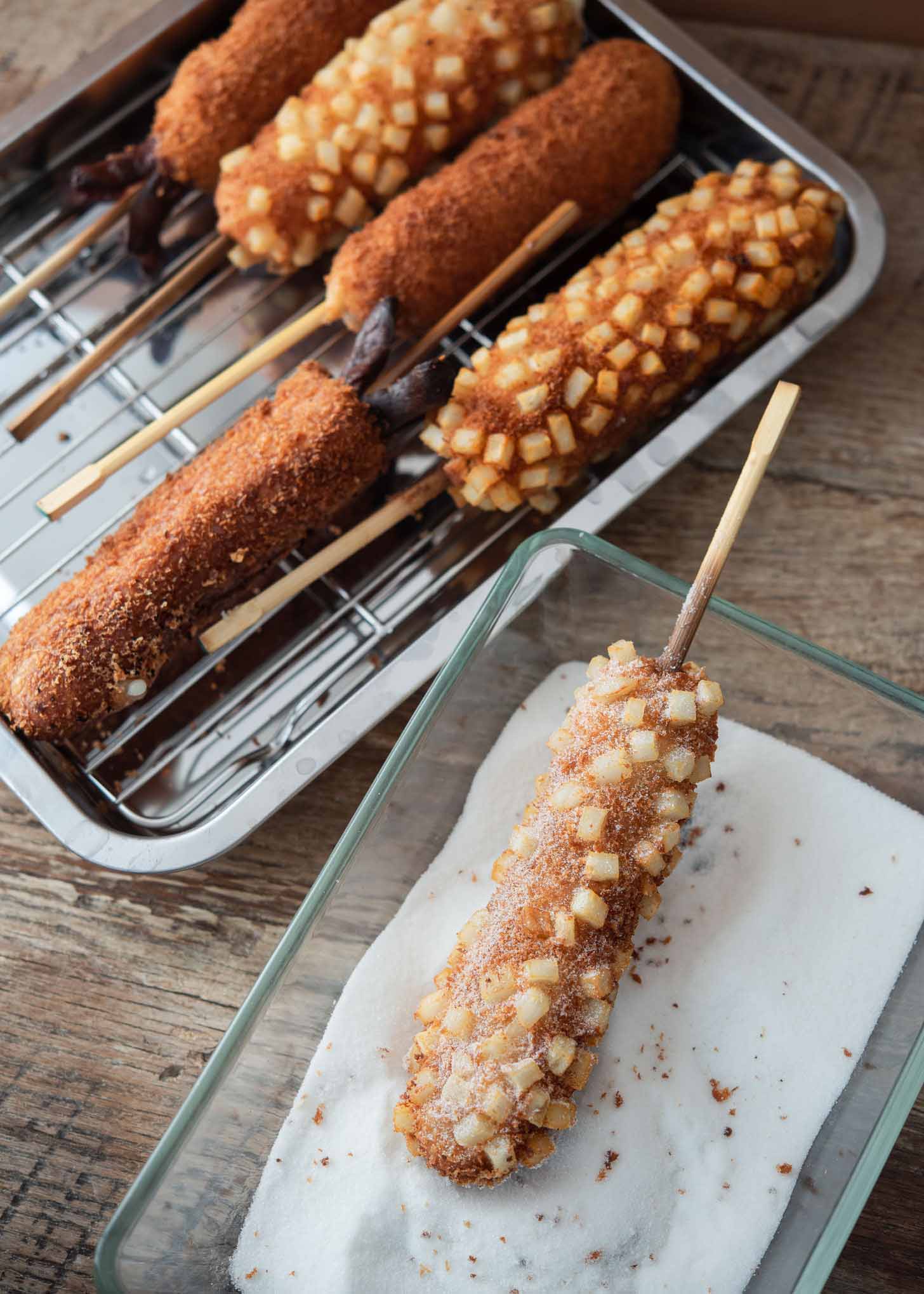 Korean hotdog fried with potato being dusted with sugar.