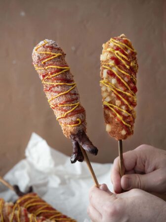 Two Korean corn dogs on sticks held up.