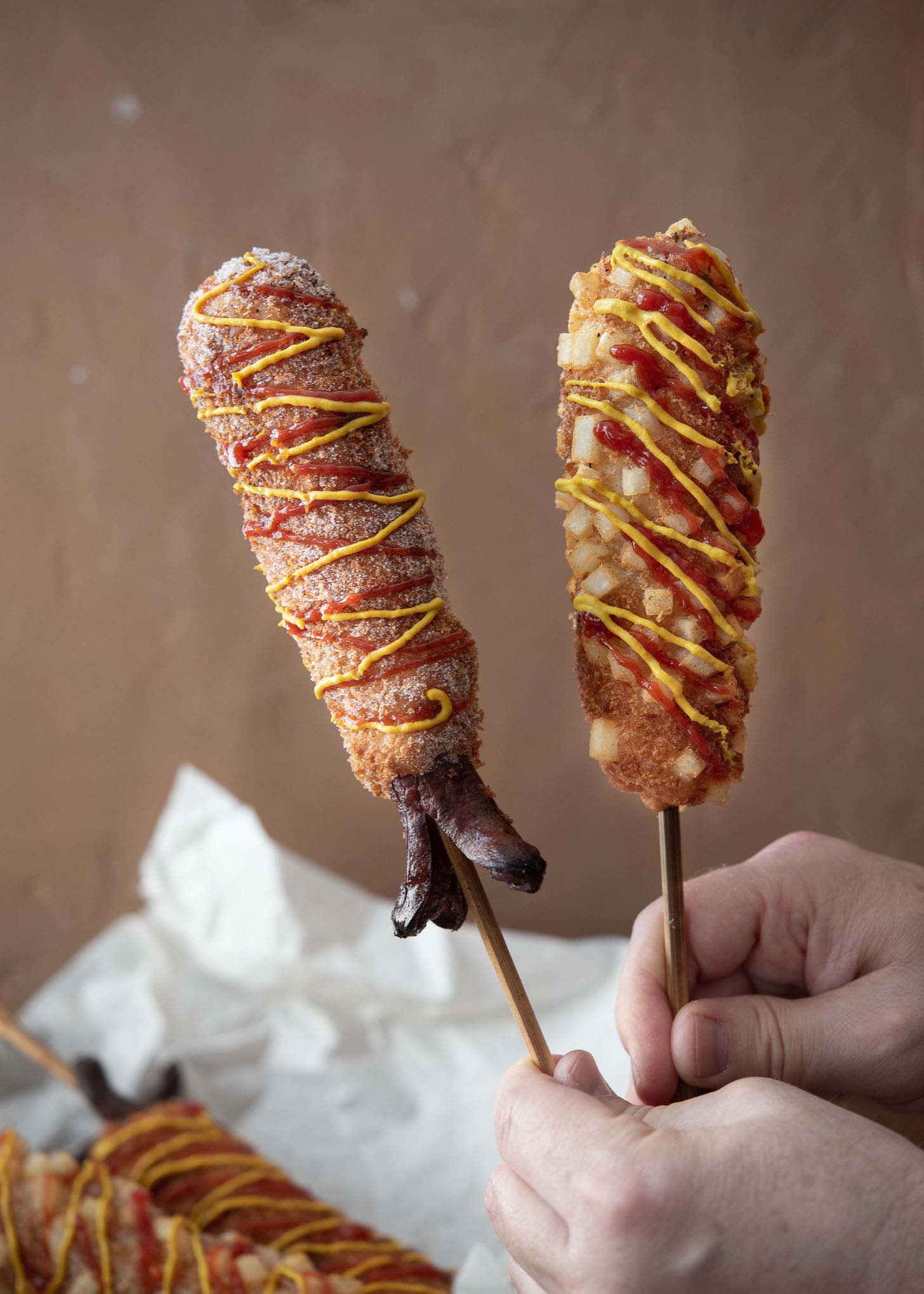 Two Korean corn dogs on sticks held up.