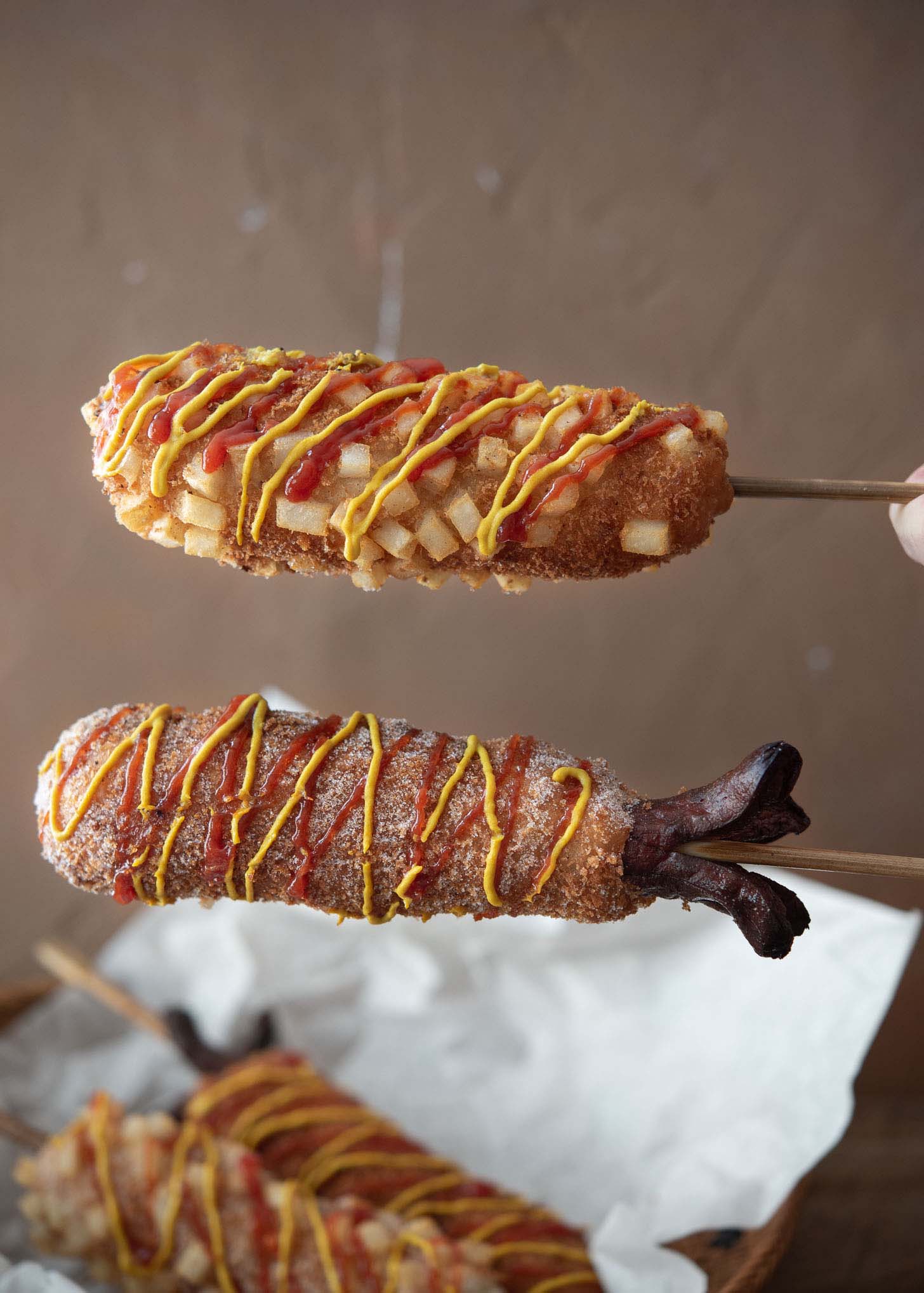 Two Korean corn dogs drizzled with ketchup and mustard.