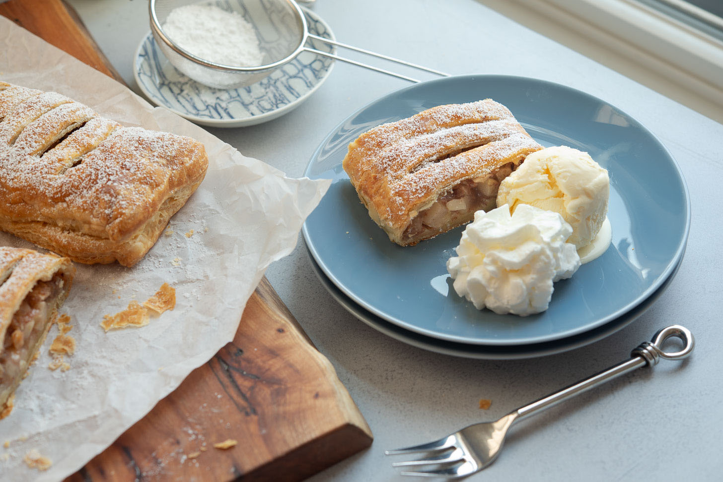 A slice of apple strudel served with ice cream and whipped cream on a plate
