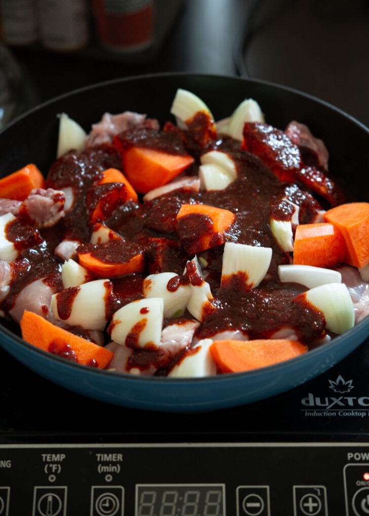 Spicy seasoning sauce added to chicken and carrot in a pan.