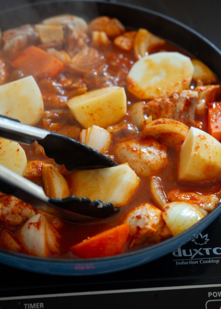 Potato chunks are added to simmering chicken stew in a pan.