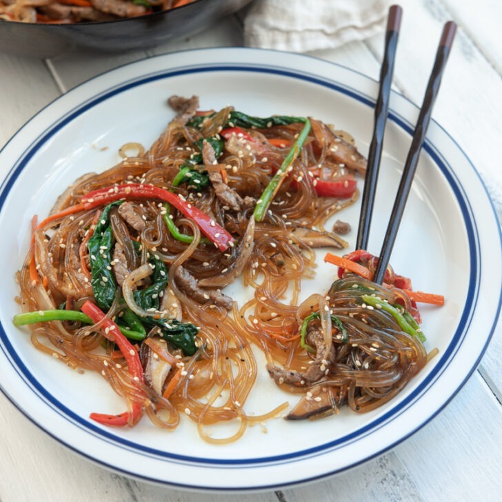 A plate of japchae glass noodles with vegetables and beef.