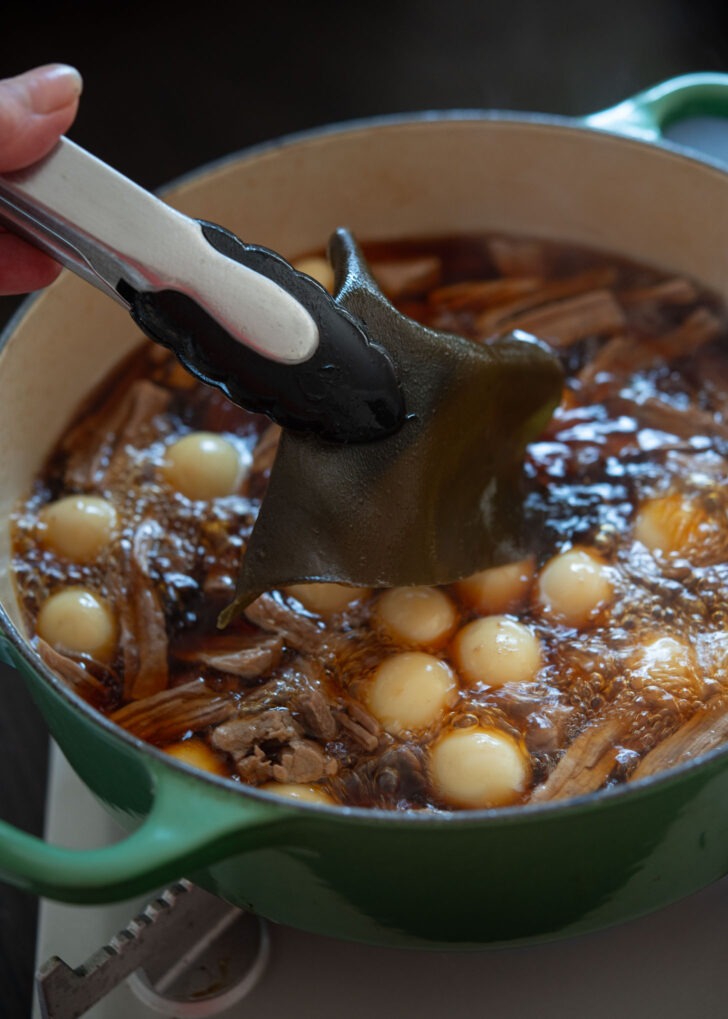 Removing sea kelp from simmering soy braised beef in a pot.