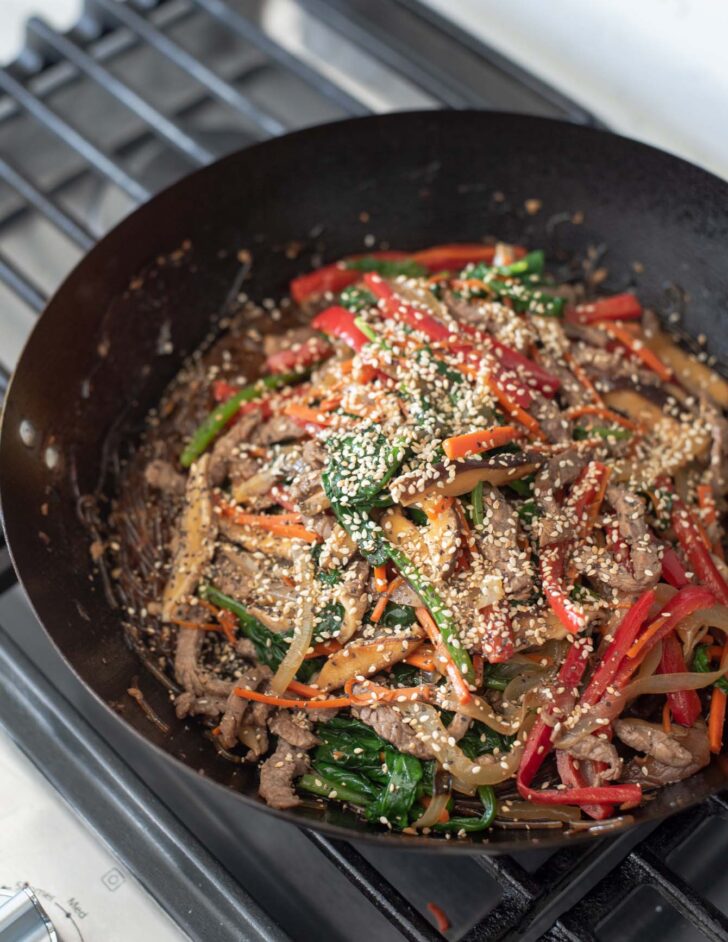 Extra seasoning added to glass noodle stir-fry in a skillet.