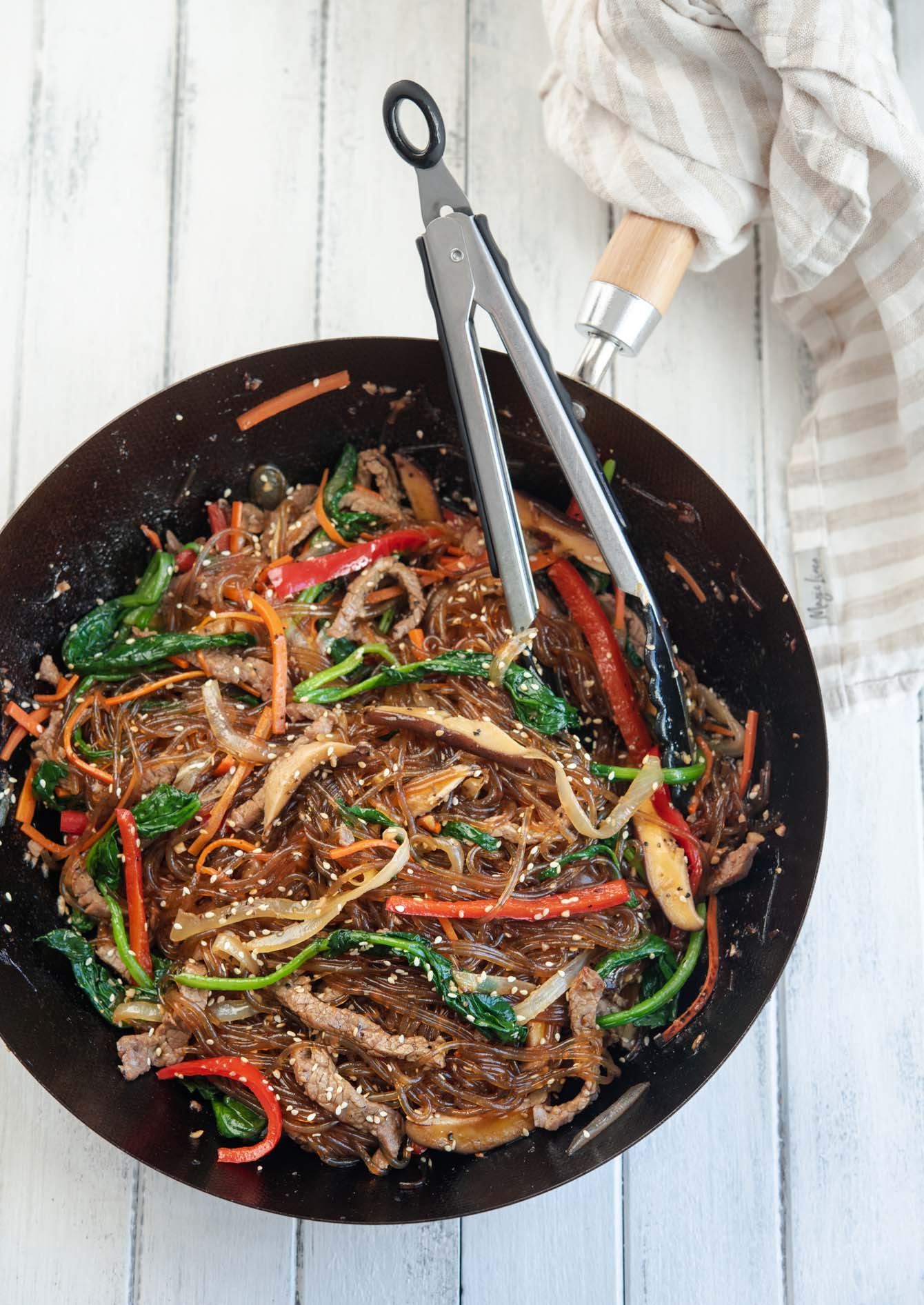 A pot of Korean glass noodle stir-fry with kitchen tongs.