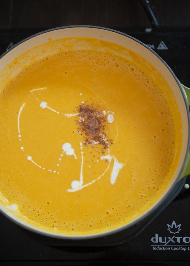 Cream and nutmeg added to kabocha squash soup in a pot.