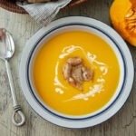 A bowl of kabocha squash soup garnished and served with crusty bread.