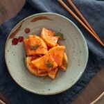 Korean radish kimchi, kkakdugi, served in a bowl with chopsticks.