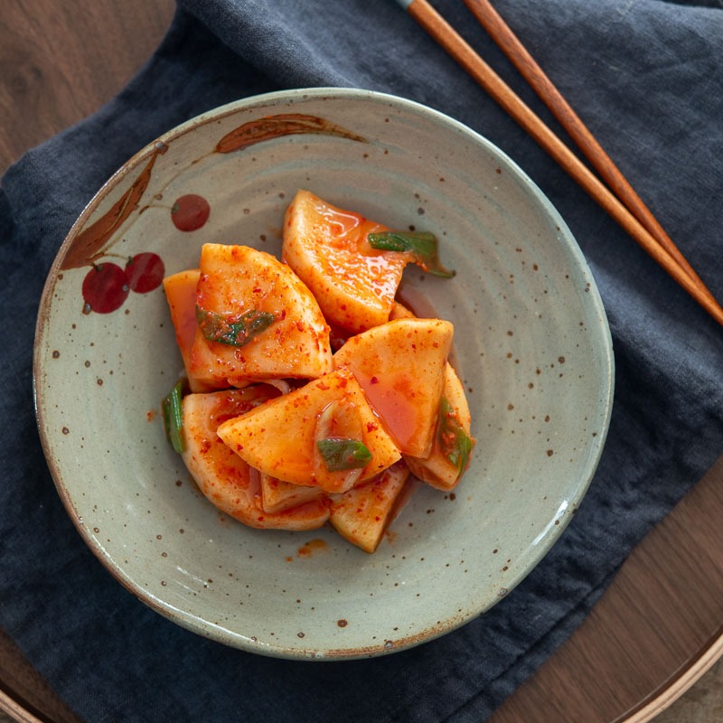 Korean radish kimchi (kkakdugi) in a serving dish with chopsticks on the side.