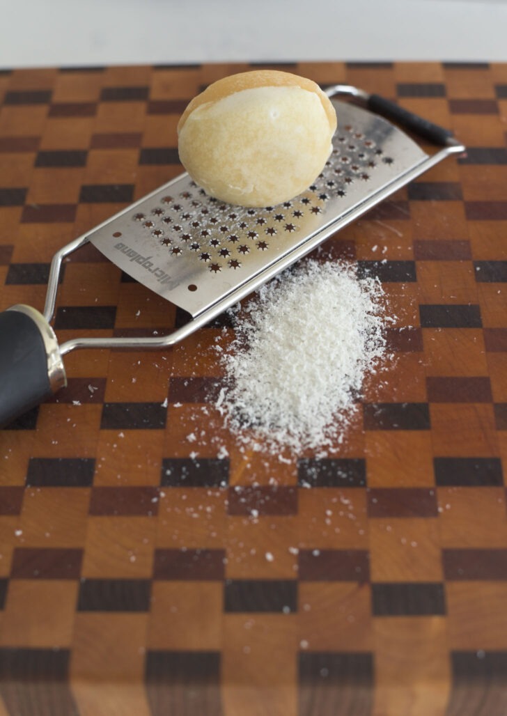Palm sugar grated over a grater on a working surface.