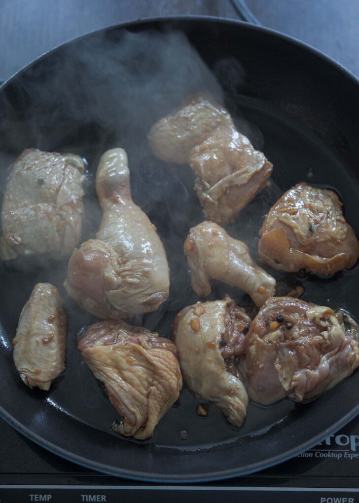 Marinated adobo chicken pieces sizzling on a hot skillet.