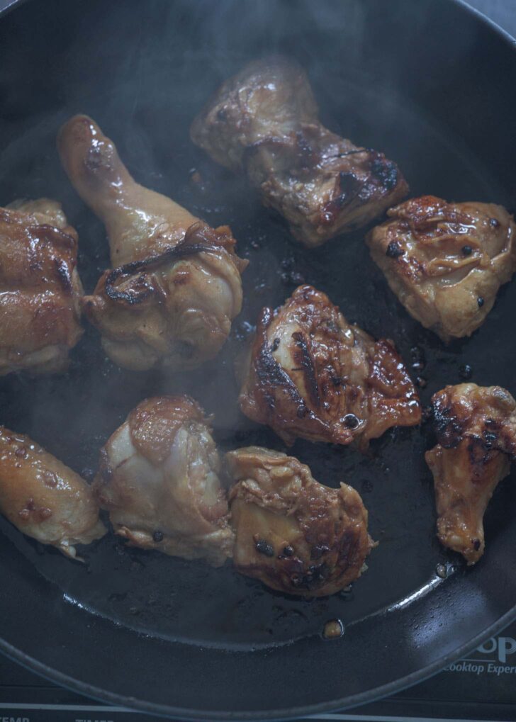 Marinated adobo chicken browned on a skillet.