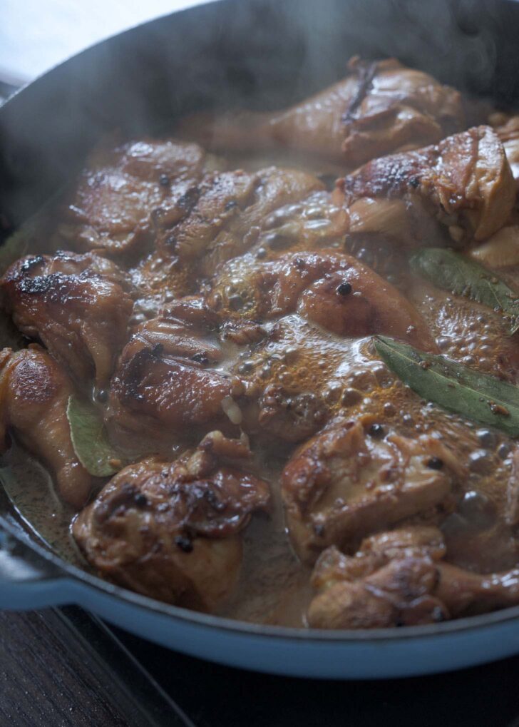 Chicken pieces boiling in adobo sauce mixture.