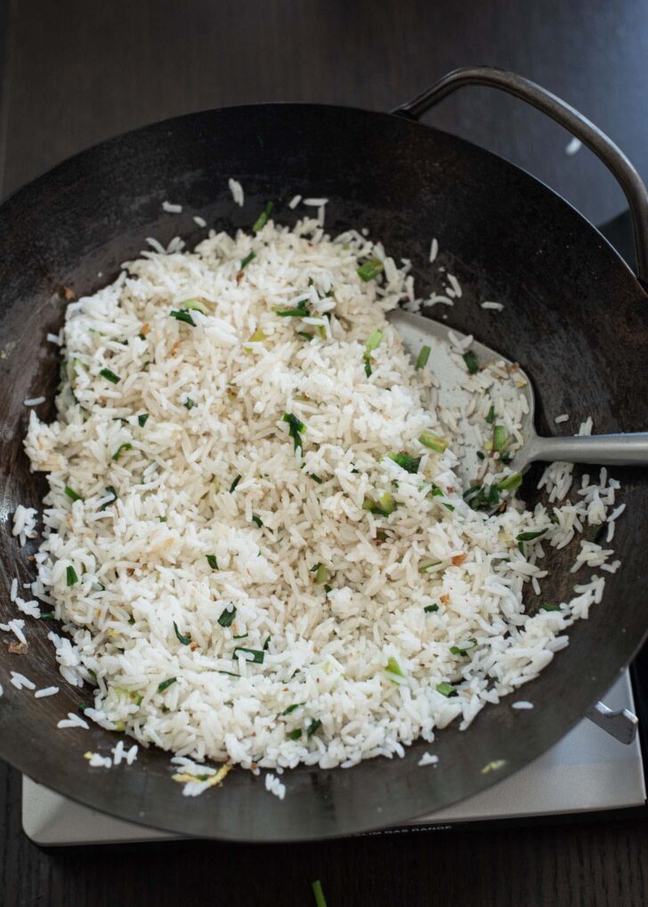 White rice stir-frying with aromatics in a wok.