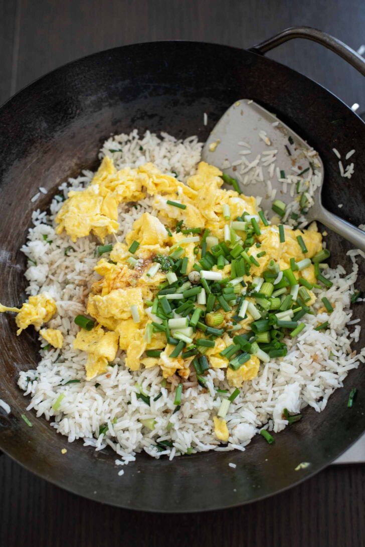 Scrambled egg and green onion added to the fried rice in a wok.