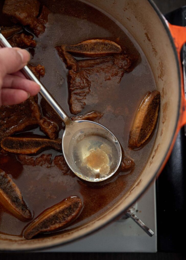 A spoon skimming off extra fat on top of braising liquid.