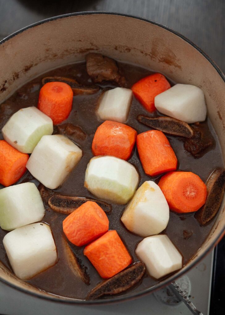 Carrots and radishes added to braised short ribs in a pot.