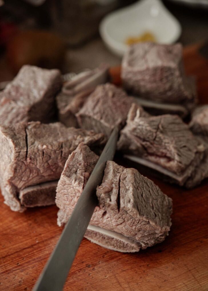 Knife scoring a few slits on top of short rib meats.