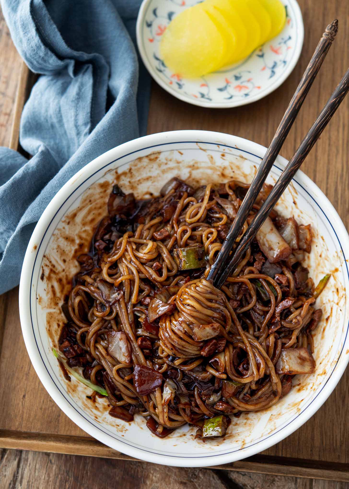 A pair of chopsticks is twirling black bean noodles in a bowl.