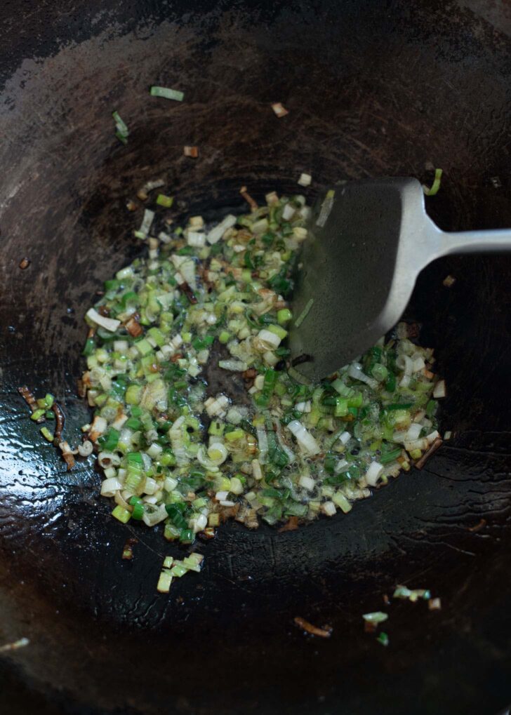 Chopped green onion stir fried with lard in a wok.