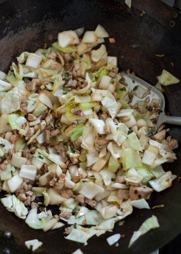 Cabbage and onion are stir frying with pork in wok.