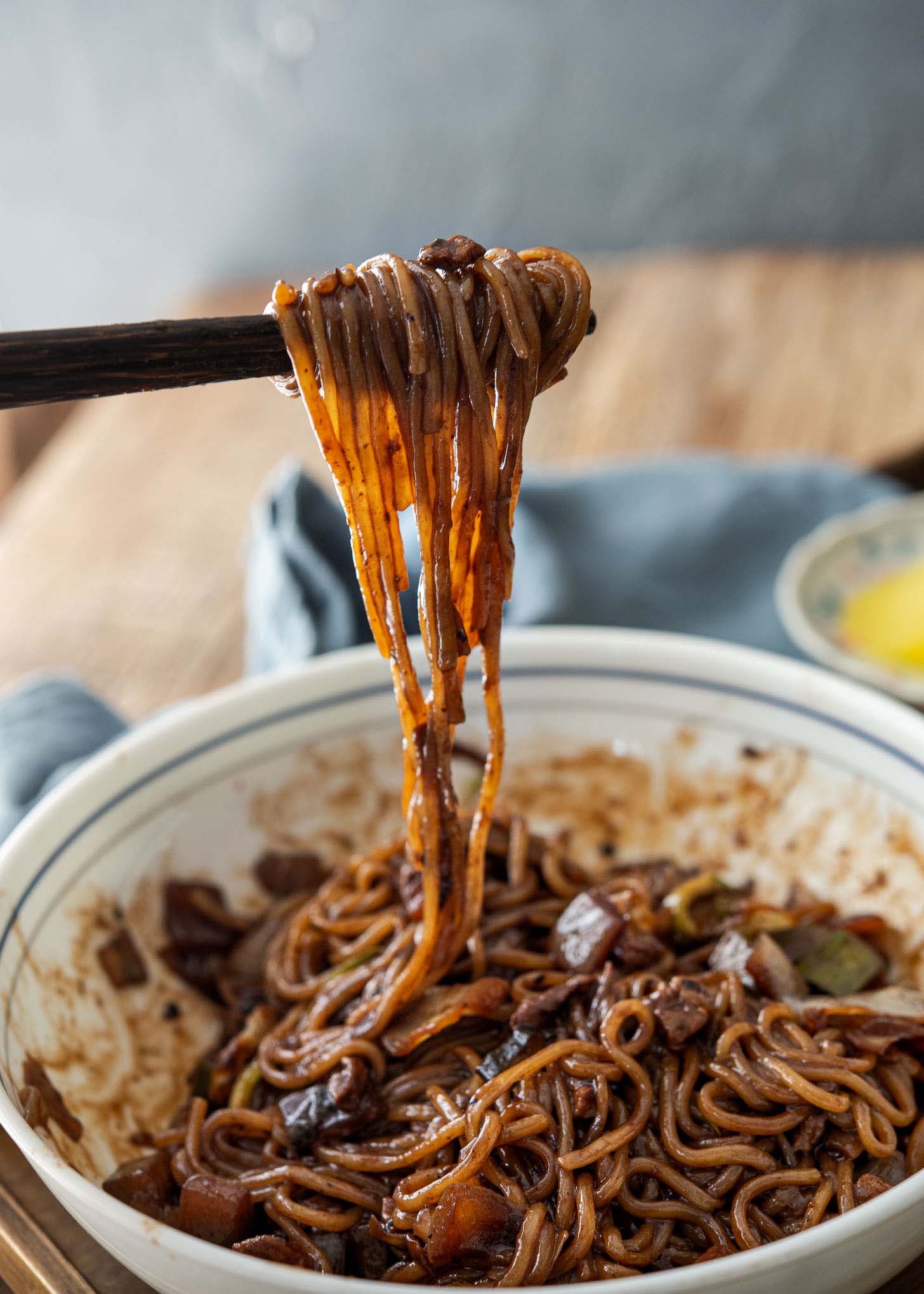 A pair of chopsticks holding up black bean noodles.