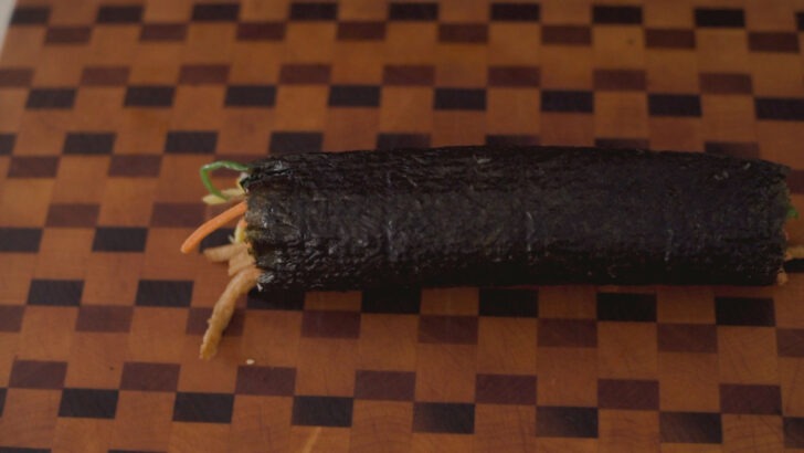 One roll of finished kimbap on the cutting board.