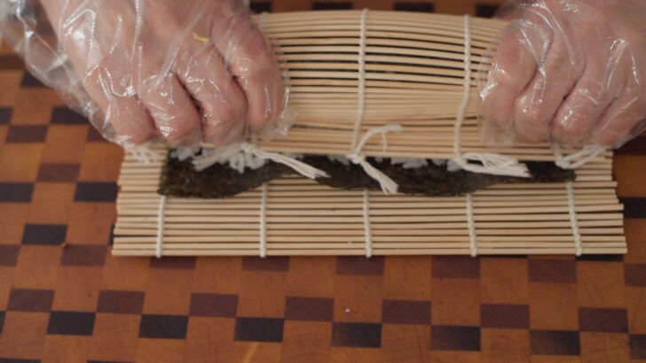 Squeezing the bamboo mat tightly after to secure kimbap inside.