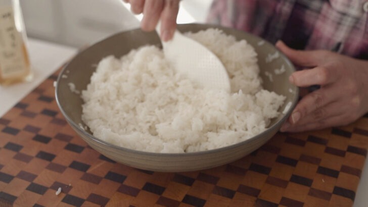 Cooked rice seasoned with plum extract in a large mixing bowl.