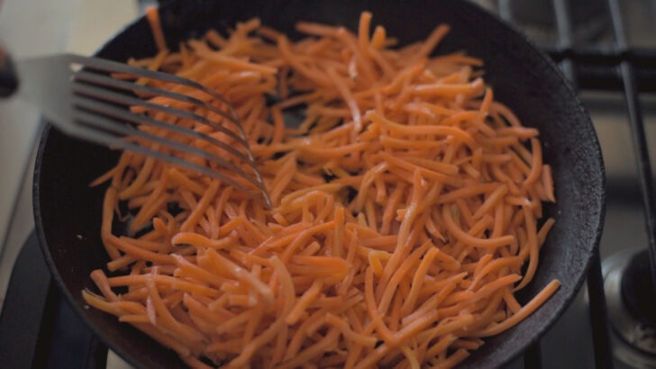 Shredded carrots are cooking in a skillet.
