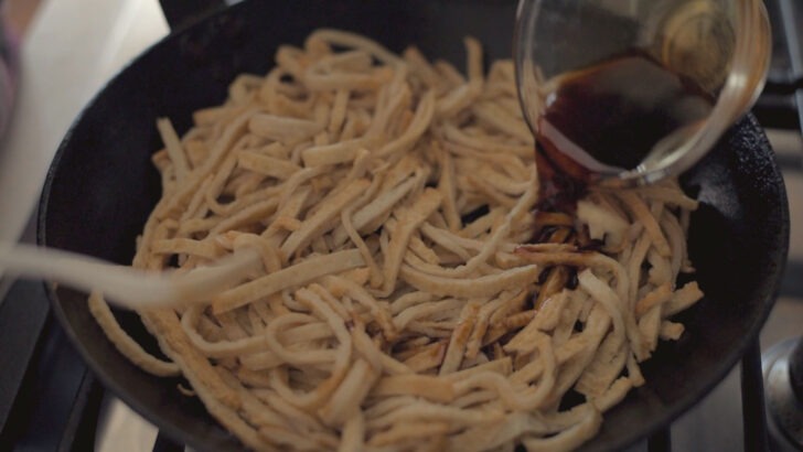 Fish cake strips seasoned with soy sauce in a skillet.