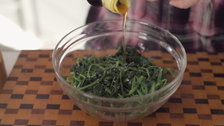 Sesame oil added to spinach in a bowl.