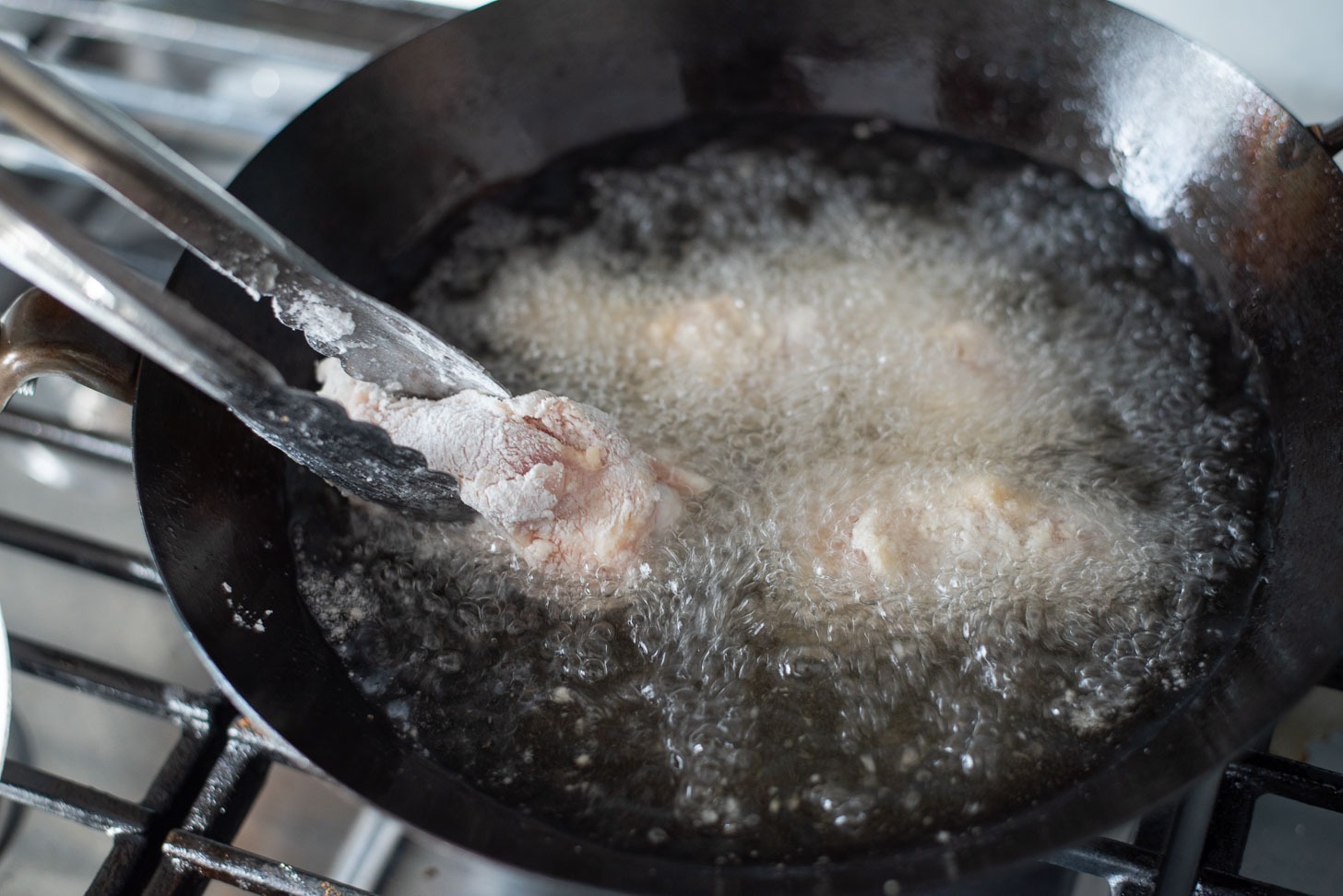Chicken wings enters hot oil for deep frying.