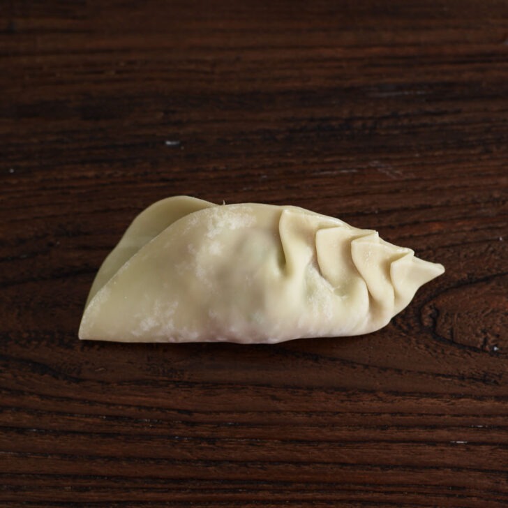 More pleats are pinched toward the center of dumpling.