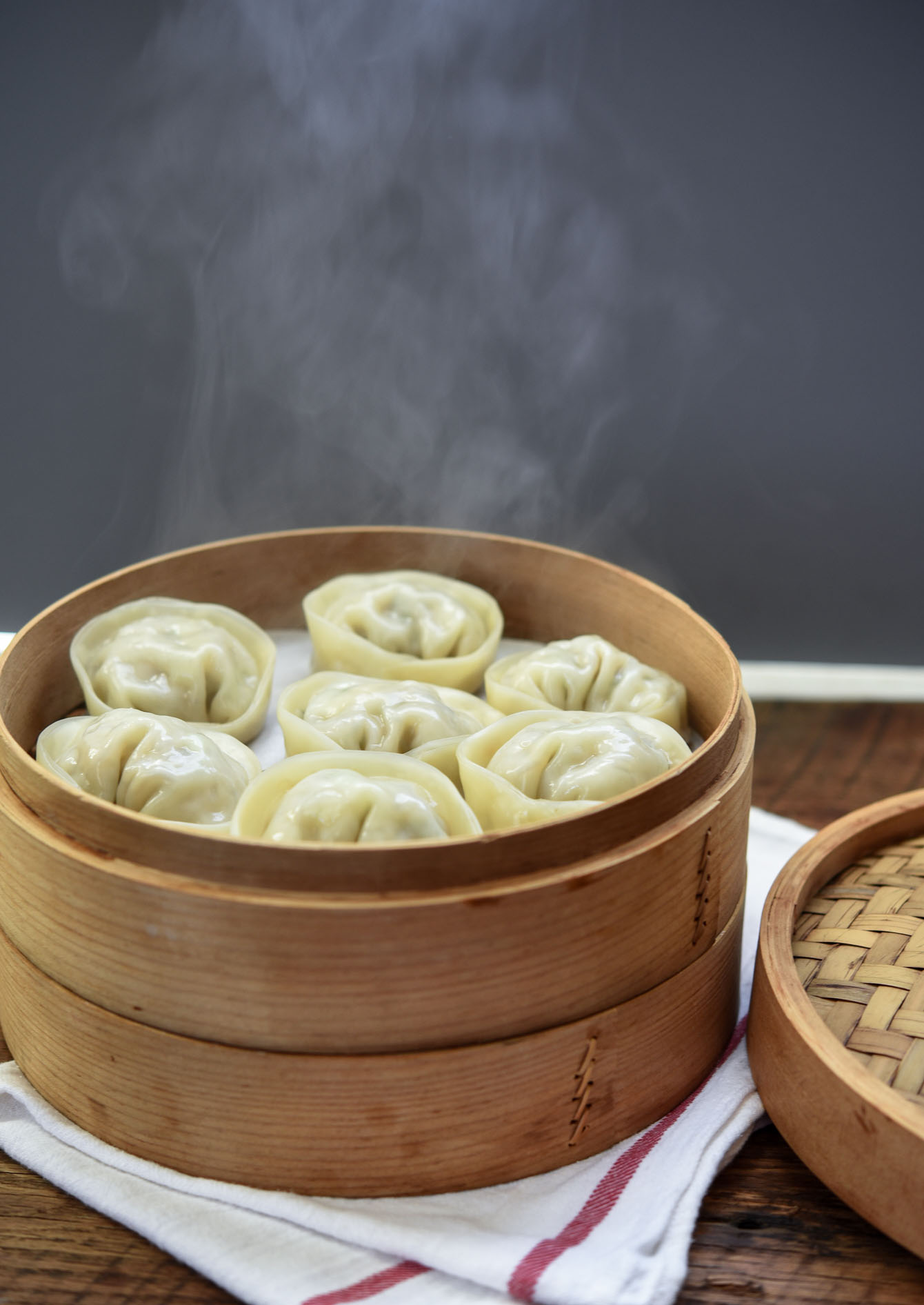 Steam coming up from cooked Korean dumplings in a bamboo steamer.