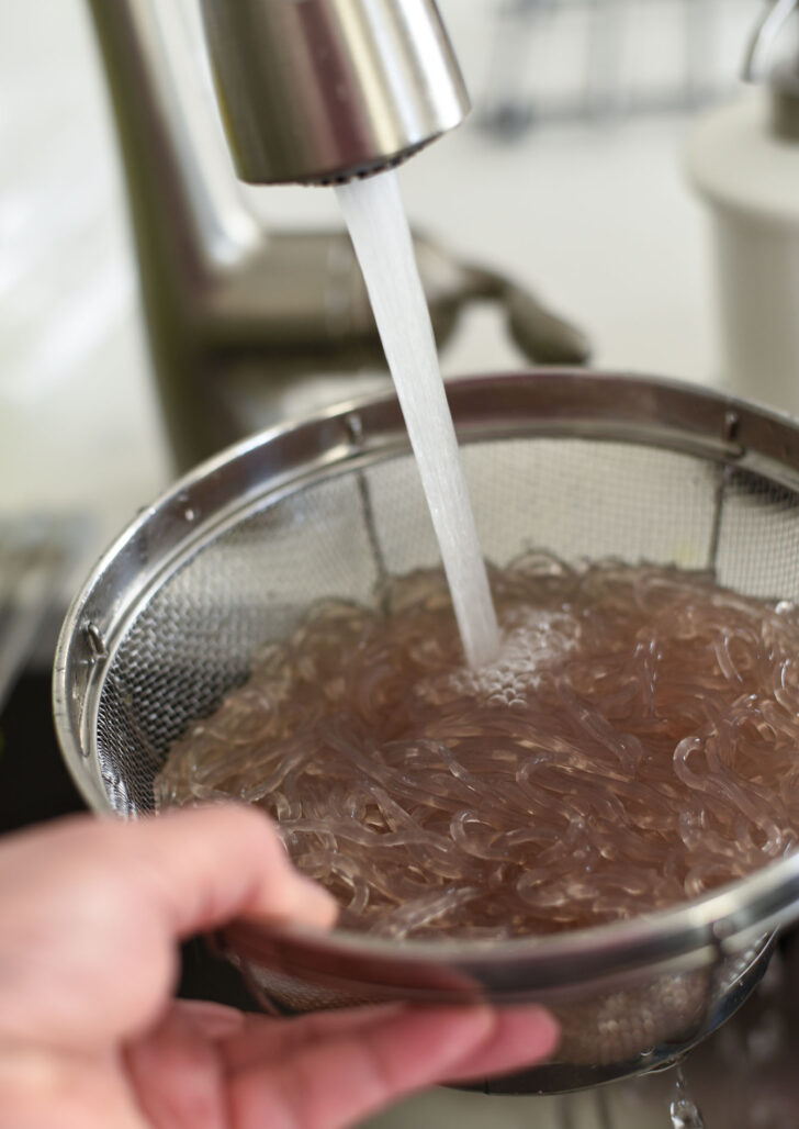 Cooked Korean glass noodles rising under running water.